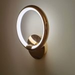 Gold ring round wall light switched on — cool white LED glow on wall, close-up installation shot