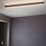 Black linear wall light mounted at ceiling line casting warm white light across ceiling
