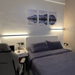 Black linear wall light installed horizontally on bedroom wall beside bed