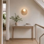 Round travertine wall light above console table in hallway stairway with warm ambient glow and wabi sabi styling