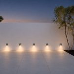 Grey LED step lights mounted in a row along an outdoor boundary wall at dusk